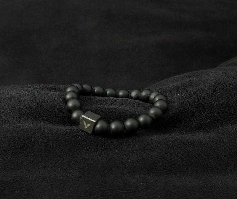 Black beaded bracelet with a hexagonal metal clasp on a black fabric background