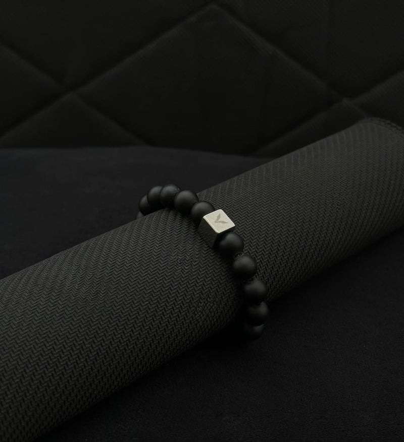 Black beaded bracelet with a silver clasp on a black fabric background